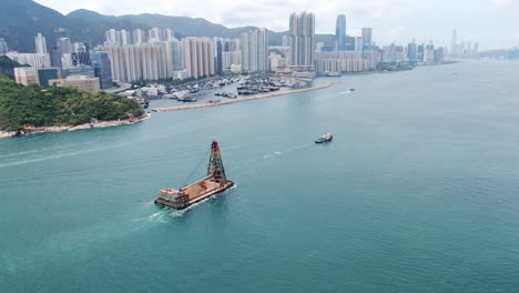 tugboat pulling a barge loaded with fresh excavated sand along hong kong coastline, aerial view