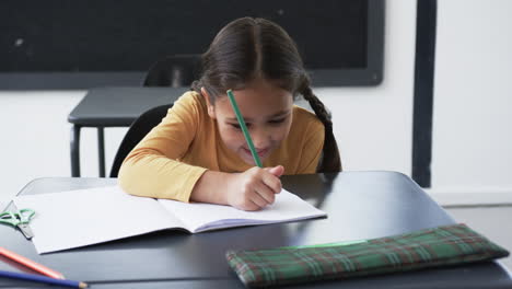 In-a-school-setting,-a-young-biracial-girl-focuses-on-writing