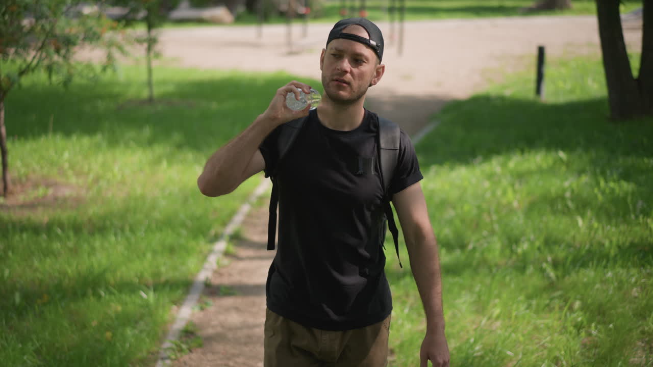 Man Opening Bottle, Man Reaches For Water Bottle In Park, Peaceful Male With Bottled Water Amid Lush Greenery, Serene Individual Opening Transparent Bottle Surrounded By Summer Foliage In Park