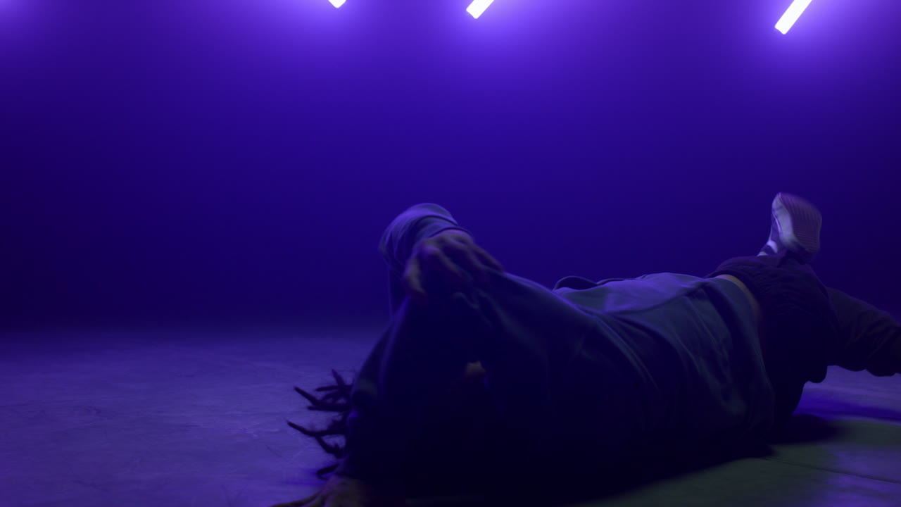 Breakdancer alla moda che muove il corpo sdraiato sulla pista da ballo in discoteca sotto luci ultraviolette.