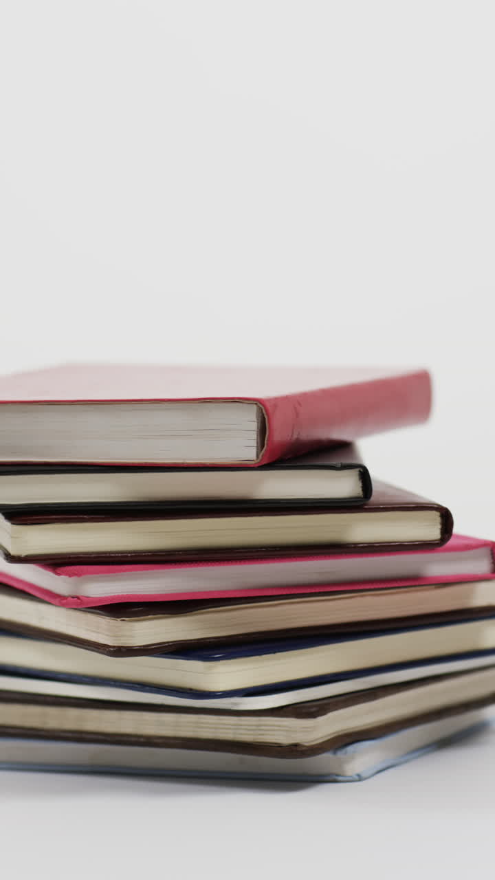 Vertical video of stack of books with copy space on grey background, in slow motion