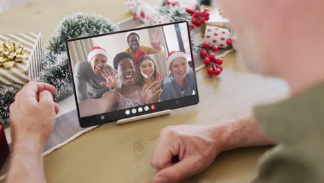 hombre caucásico con decoraciones de navidad teniendo llamada de video de tableta con amigos diversos felices