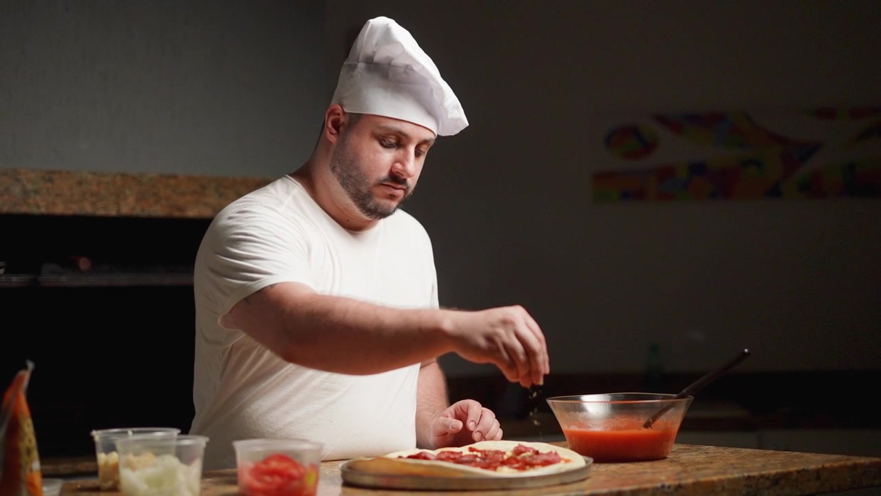 Filmato al rallentatore di uno chef che aggiunge origano fresco a una pizza al salame piccante calda e croccante
