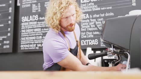 barista caucásico limpiando la máquina de café con un paño en la cafetería
