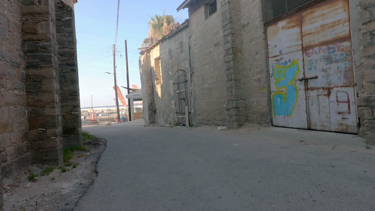 Wandering Zygi village’s quiet backstreets in Cyprus—stone buildings with old wooden and metal doors, leading toward the harbor in the distance. A blend of rustic charm and coastal beauty.