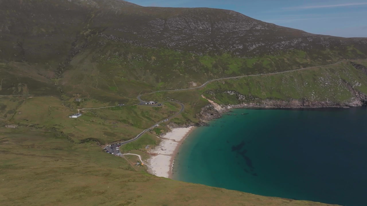 A stunning cinematic aerial shot of Keem Beach on Achill Island, featuring turquoise water, white sand, and lush green cliffs. Captures the authentic beauty of the Irish coastline.
