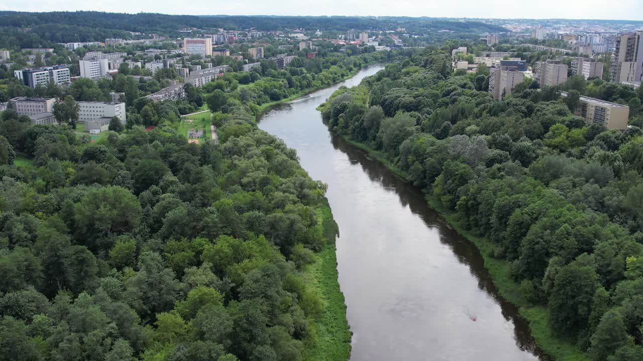 Sorvolo aereo del fiume Neris a Vilnius, con un corso d'acqua tortuoso fiancheggiato da una fitta vegetazione estiva e quartieri residenziali che si estendono attraverso la capitale