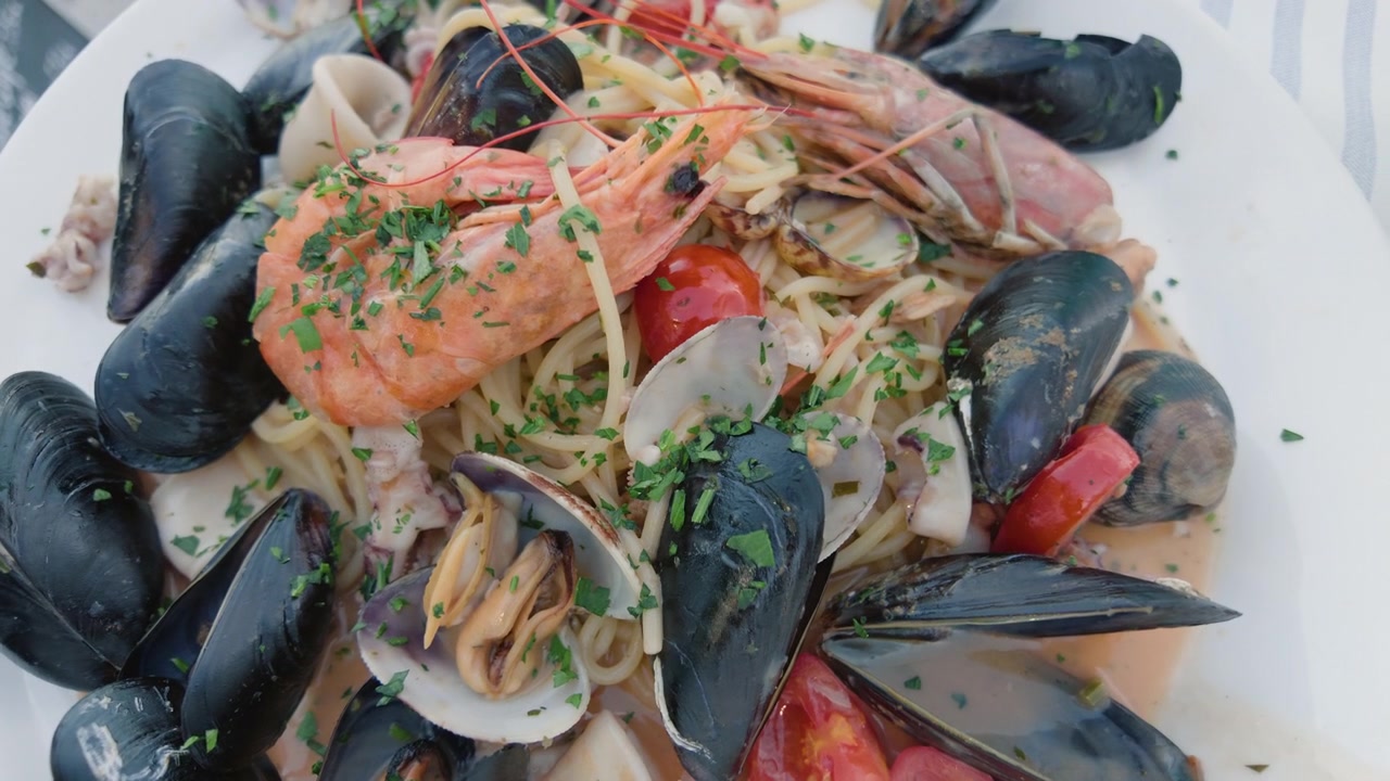Primo piano di una pasta ai frutti di mare con cozze, vongole, gamberi e pomodorini su un piatto bianco