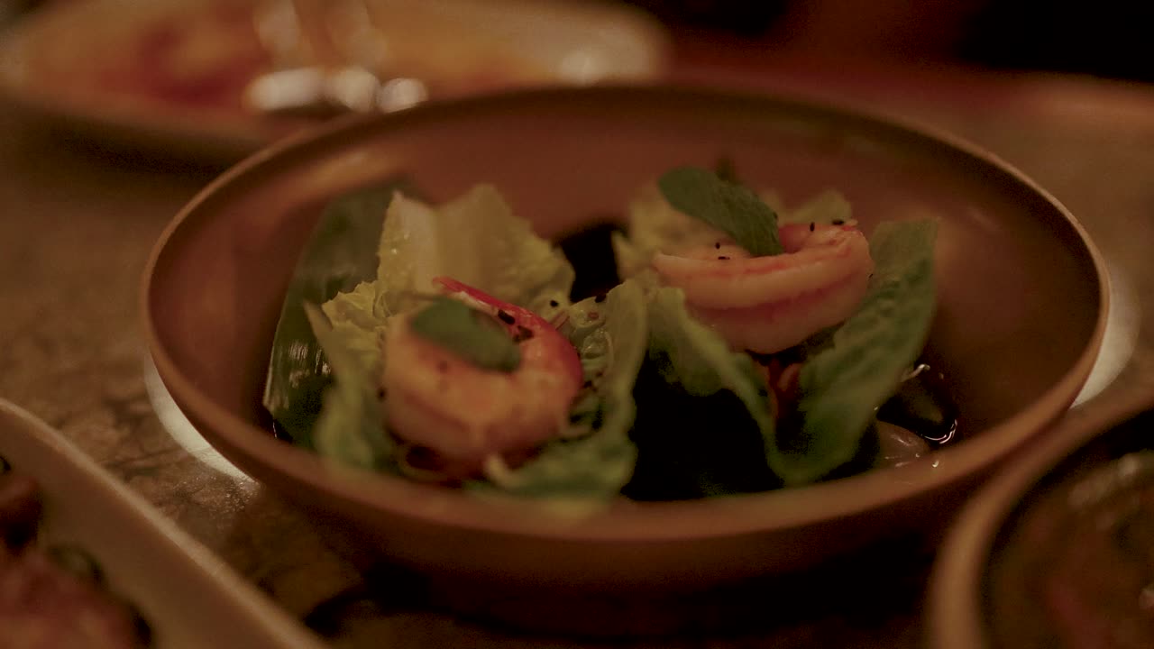 Close-up of shrimp miang kham on a wooden plate under warm, ambient lighting, highlighting fresh ingredients and vibrant colors