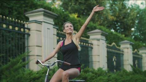 Mujer-Feliz-En-Bicicleta-En-El-Parque-De-La-Ciudad.-Chica-En-Forma-Entrenando-En-Bicicleta-En-Verano