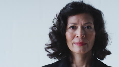 portrait of determined mature businesswoman in suit standing against white studio wall