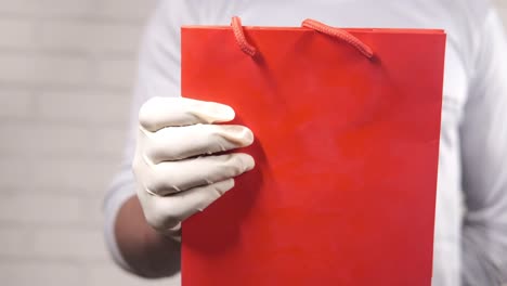 persona con guantes blancos sosteniendo una bolsa de compras roja