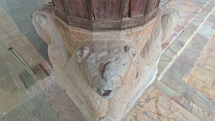 Primo piano di antica scultura di leone in pietra che sostiene una colonna di legno