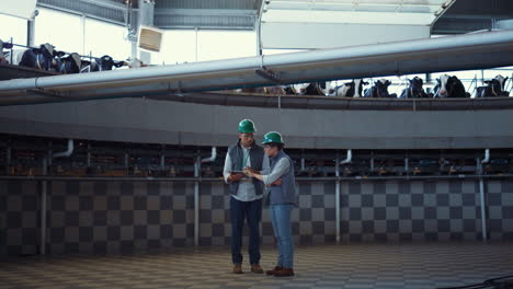 dairy farm workers checking documents on milking parlor equipment together.