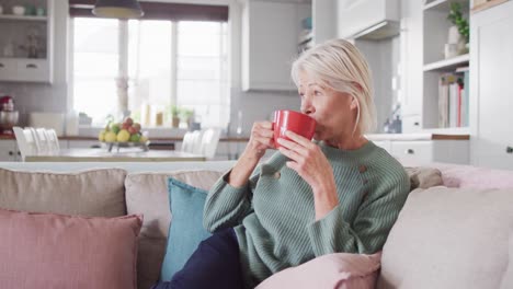 Mujer-Caucásica-Mayor-Pensativa-Sentada-En-Un-Sofá-En-La-Sala-De-Estar,-Bebiendo-Café