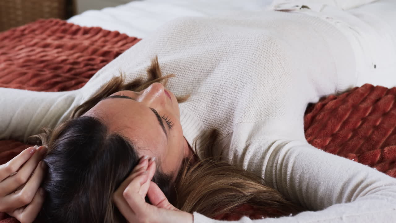 Relaxing at home, woman lying on bed in cozy sweater, feeling peaceful