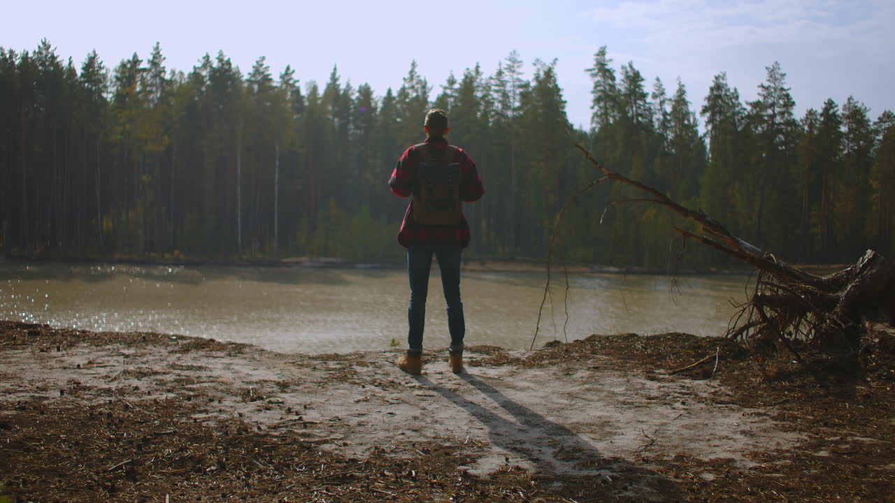 Hiker with a backpack at sunset on the top of a mountain enjoying the sunset with a raised hand in a winner's pose against the background of the river. Travel and vacation concept. High quality 4k footage