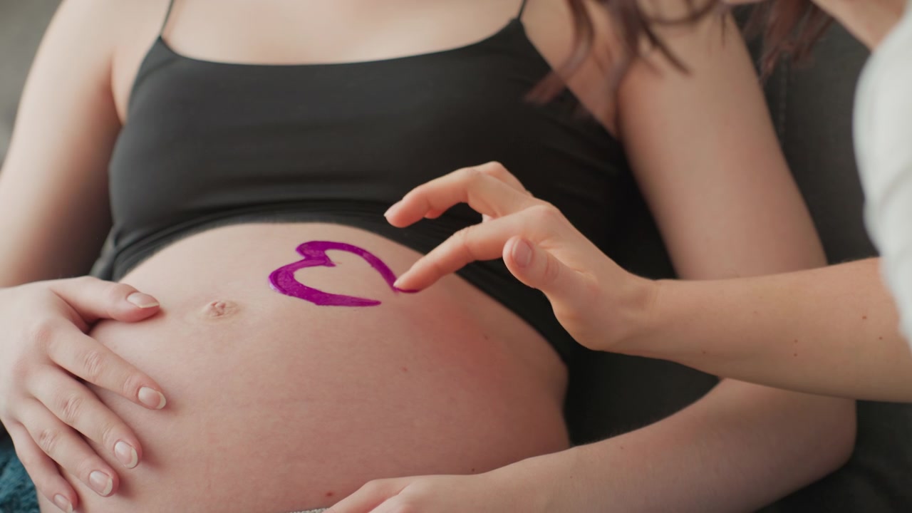 Primo piano di mani che dipingono un cuore viola su un pancione in gravidanza