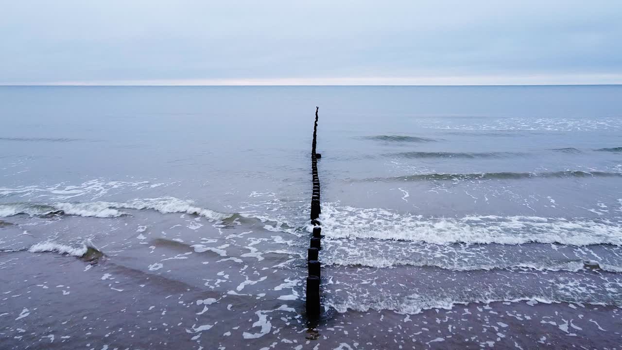 발트해 해안선에 있는 오래된 목조 부두의 아름다운 공중 전망, 흐린 날, 바다 해안 침식의 영향을 받은 백사장, 잔잔한 해변, 앞으로 움직이는 광각 드론 샷