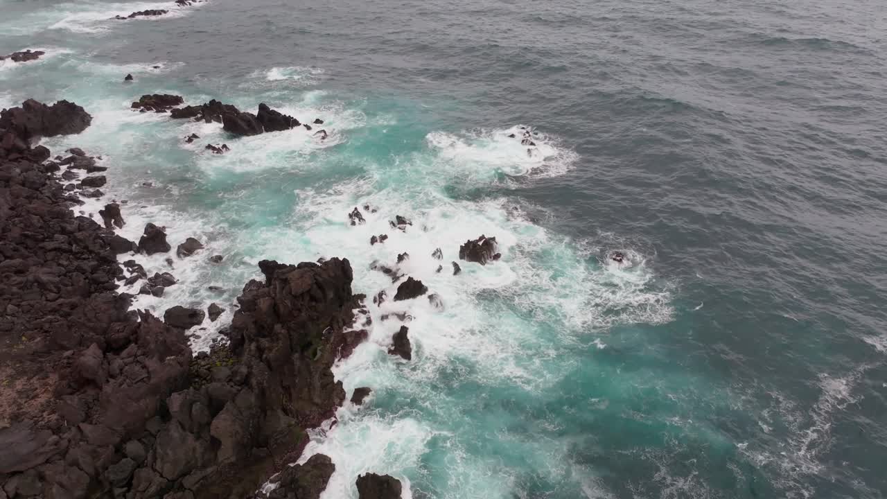 Pemandangan udara garis pantai Bretanha yang gelap dan terjal bertemu dengan perairan Atlantik berwarna pirus cerah, menciptakan kontras tekstur dan warna yang mencolok.