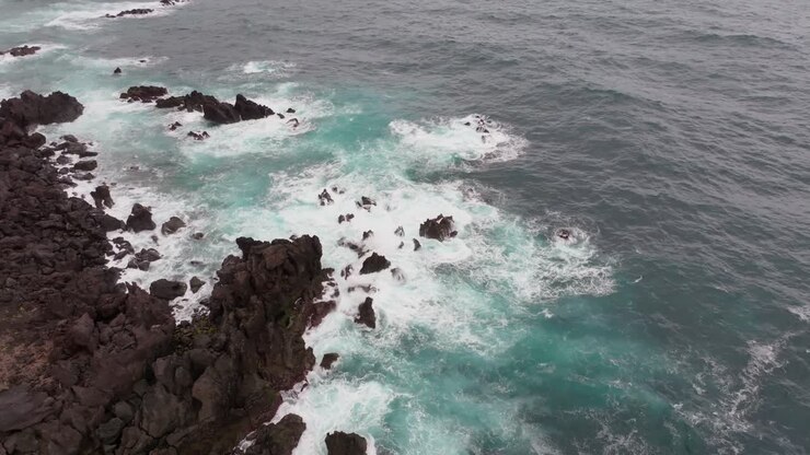Vista aerea della frastagliata costa scura della Bretagna che incontra le vibranti acque atlantiche color verde acqua, creando un sorprendente contrasto di texture e colori.