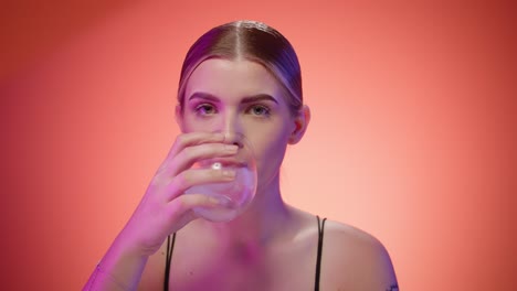 una mujer caucásica bebe agua dulce con cubitos de hielo, toma de estudio, fondo rojo