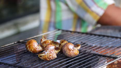 person grilling sea snails on an outdoor grill