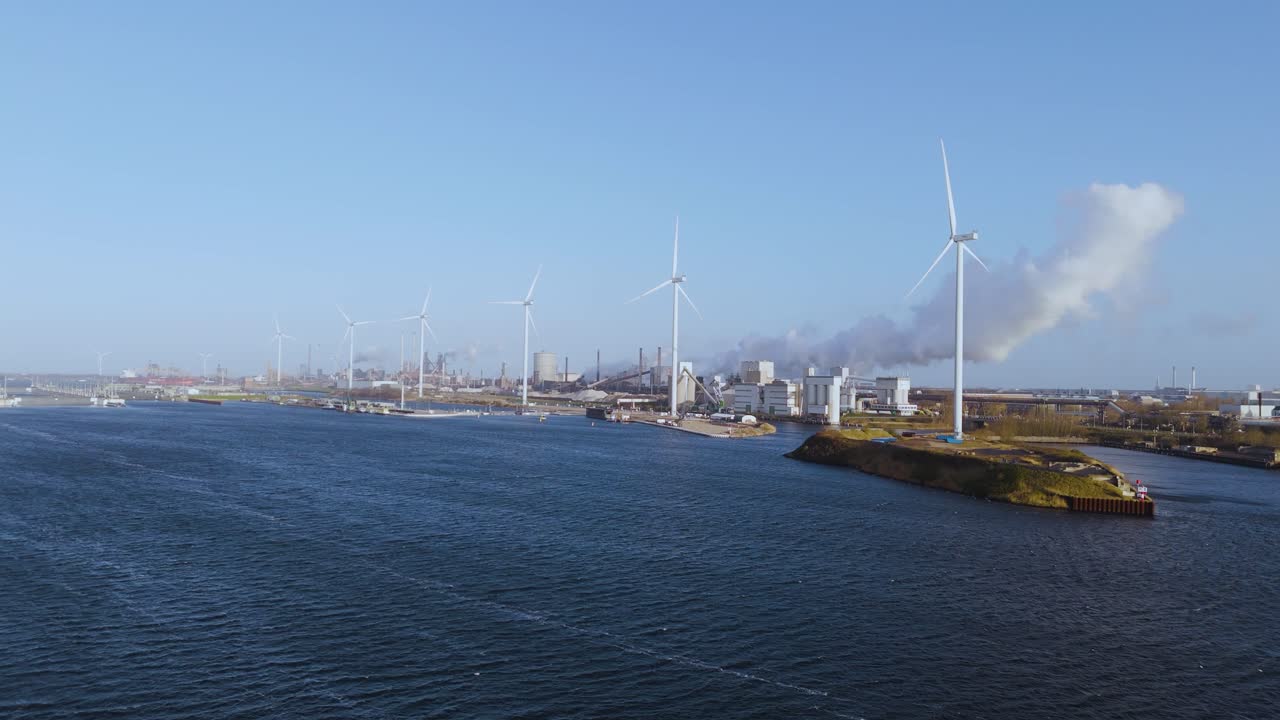 Drone aerial view of wind turbines beside an industrial harbor in the Netherlands with clear blue sky.