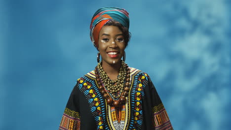 joven afroamericana alegre con turbante y maquillaje sonriendo alegremente a la cámara