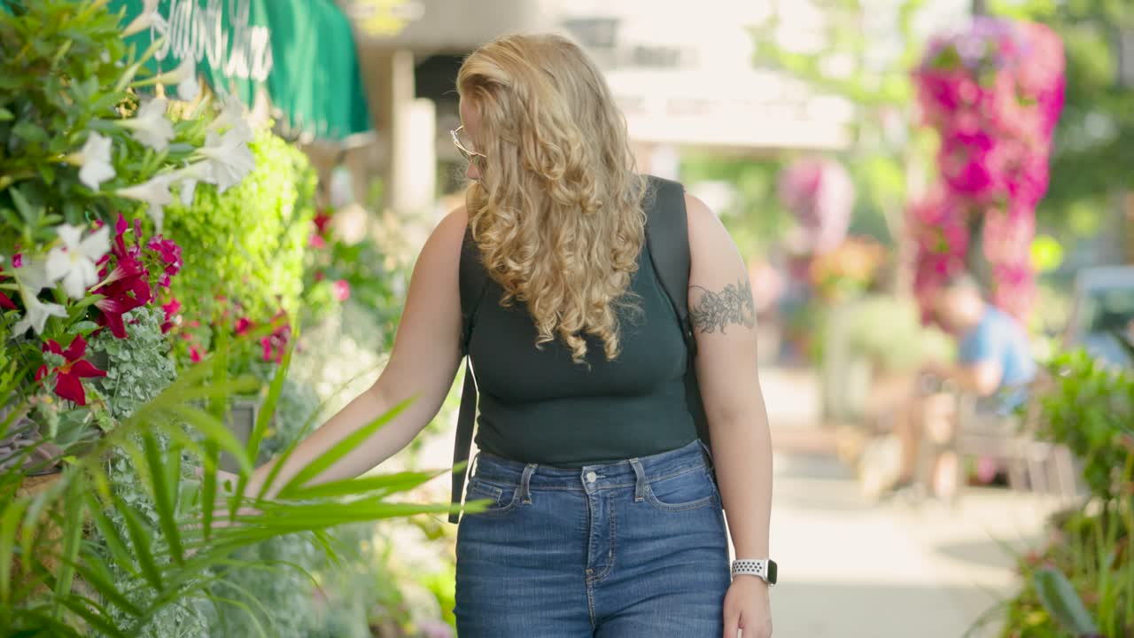 chica caminando por la acera de la ciudad mira flores y plantas