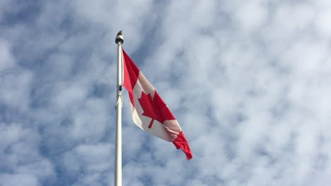 slow-motion: red and white canadian flag waving against a partially cloudy sky