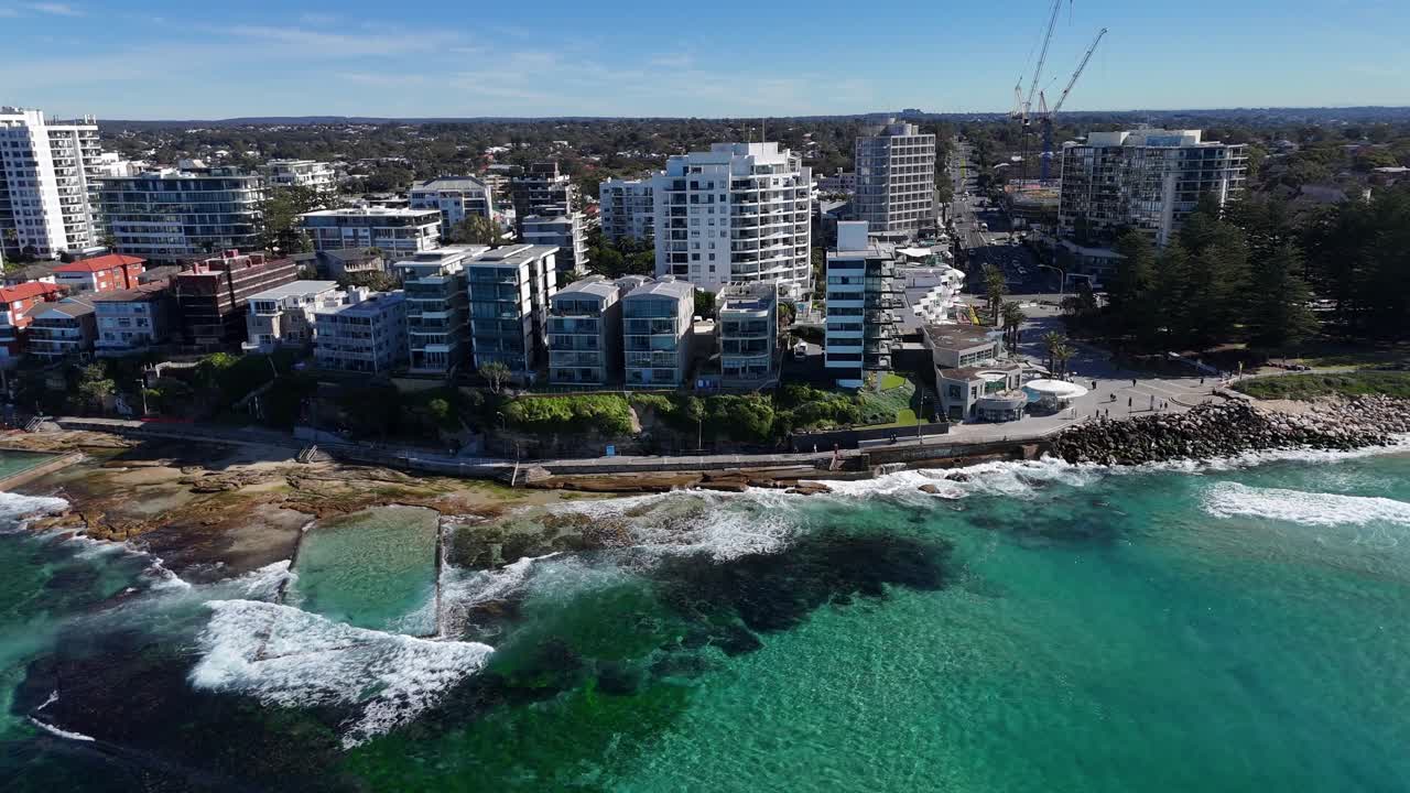 Wide aerial establishing of Cronulla shoreline with crashing waves, buildings and ocean, Sydney NSW Australia