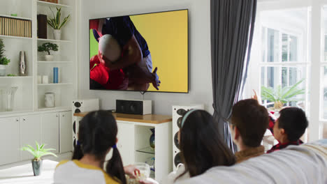 Asiatische-Familie-Vor-Dem-Fernseher-Mit-Verschiedenen-Männlichen-Rugby-Spielern,-Die-Auf-Dem-Bildschirm-Spielen