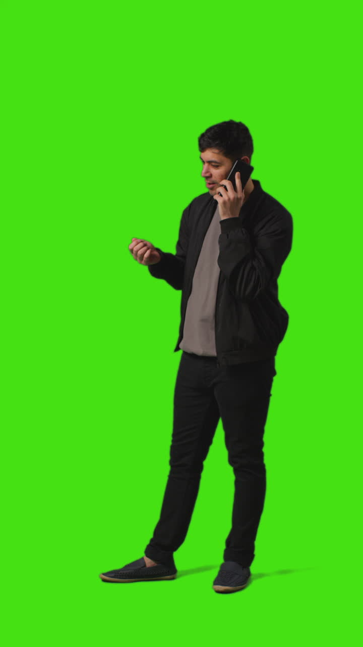 Vertical Video Full Length Shot Of Young Man Talking On Mobile Phone Standing Against Green Screen