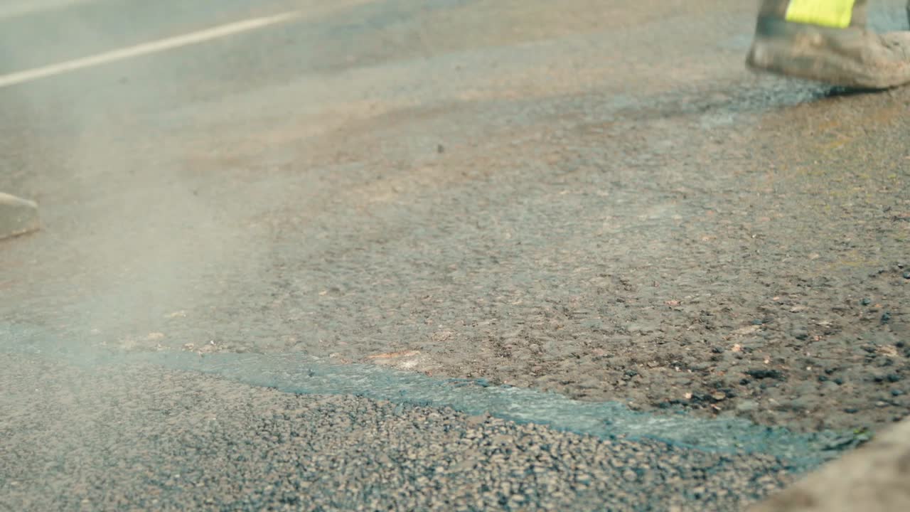 건설 노동자들이 신선한 압축 아스팔트 가장자리에 뜨거운 액체 타르를 붓고 있다