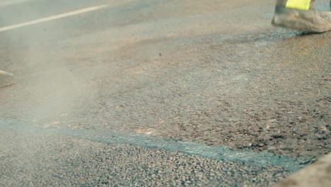 construction workers is pouring hot liquid tar on the edges of fresh compressed asphalt