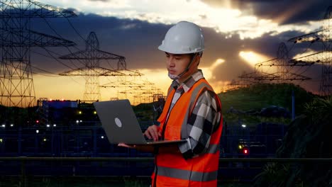 vista lateral de un ingeniero masculino asiático con casco de seguridad trabajando en una computadora portátil mientras está de pie cerca de una torre de alto voltaje