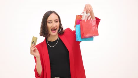 a woman in a red blazer holds shopping bags and a credit card, looking happy