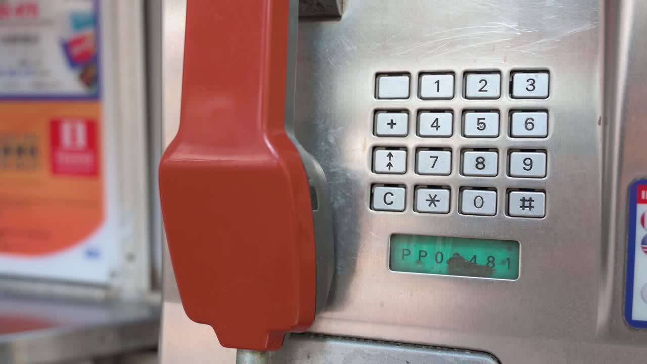 A public telephone booth, also called a payphone, with a red telephone receiver and touch-tone keypad dial is rapidly dying out and disappearing in the age of smartphones and the internet.