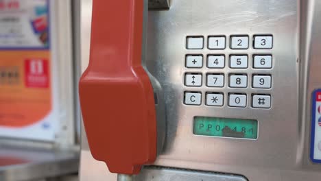 a public telephone booth, also called a payphone, with a red telephone receiver and touch-tone keypad dial is rapidly dying out and disappearing in the age of smartphones and the internet.