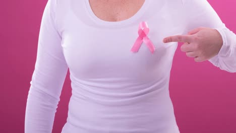 Video-of-midsection-of-caucasian-woman-wearing-pink-cancer-awareness-ribbon,-with-pink-background