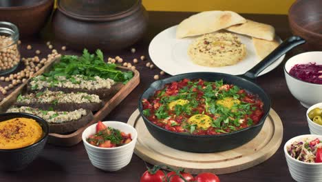 traditional israeli cuisine. shakshuka in pan decorated with parsley, forshmak and hummus on table. national jewish dishes. eggs fried in tomato sauce, dip, pita, middle eastern culture