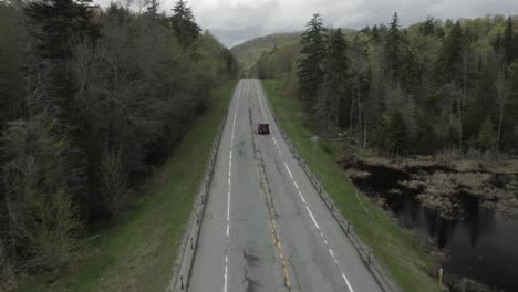drone shot, flying through the trees, with a car revealing itself from the bottom and driving away.