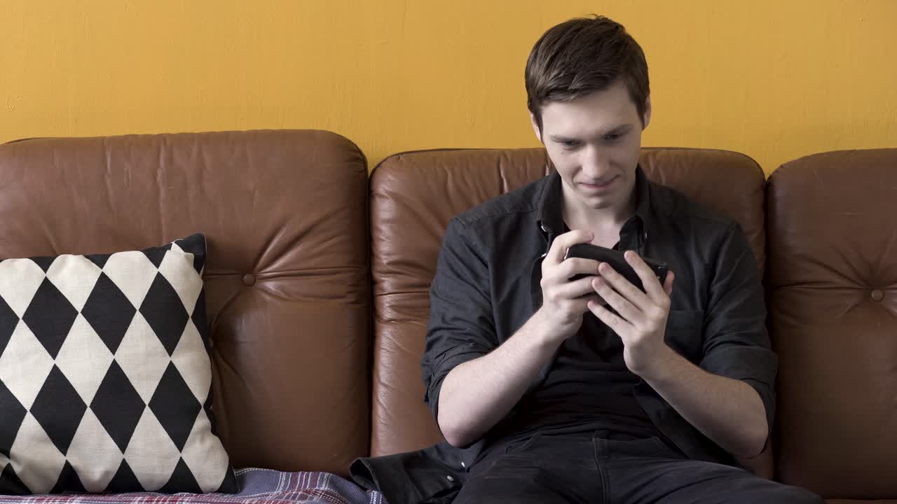 소파에서 스마트폰을 사용하는 젊은 남자