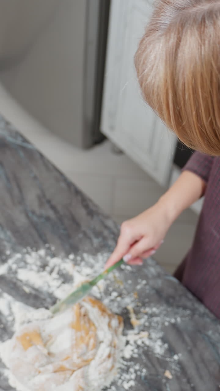 Aerial view of person kneading dough on floured tiled table in kitchen, hands work on soft, sticky dough as flour spreads across countertop, traditional homemade baking process
