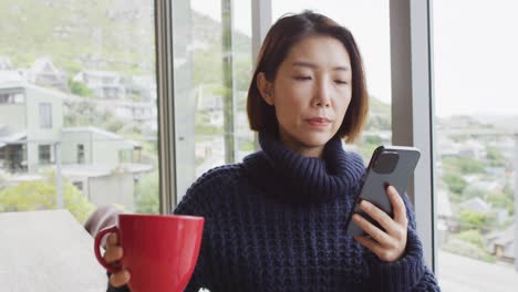 Glückliche-Asiatische-Frau,-Die-Auf-Dem-Smartphone-Spricht-Und-Im-Wohnzimmer-Sitzt