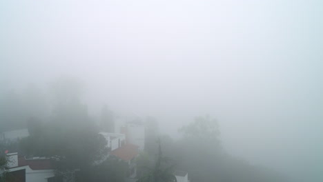 Toma-Panorámica-Que-Captura-Casas-Abrazadas-Por-Una-Densa-Niebla-En-Un-Entorno-Forestal-Sereno.