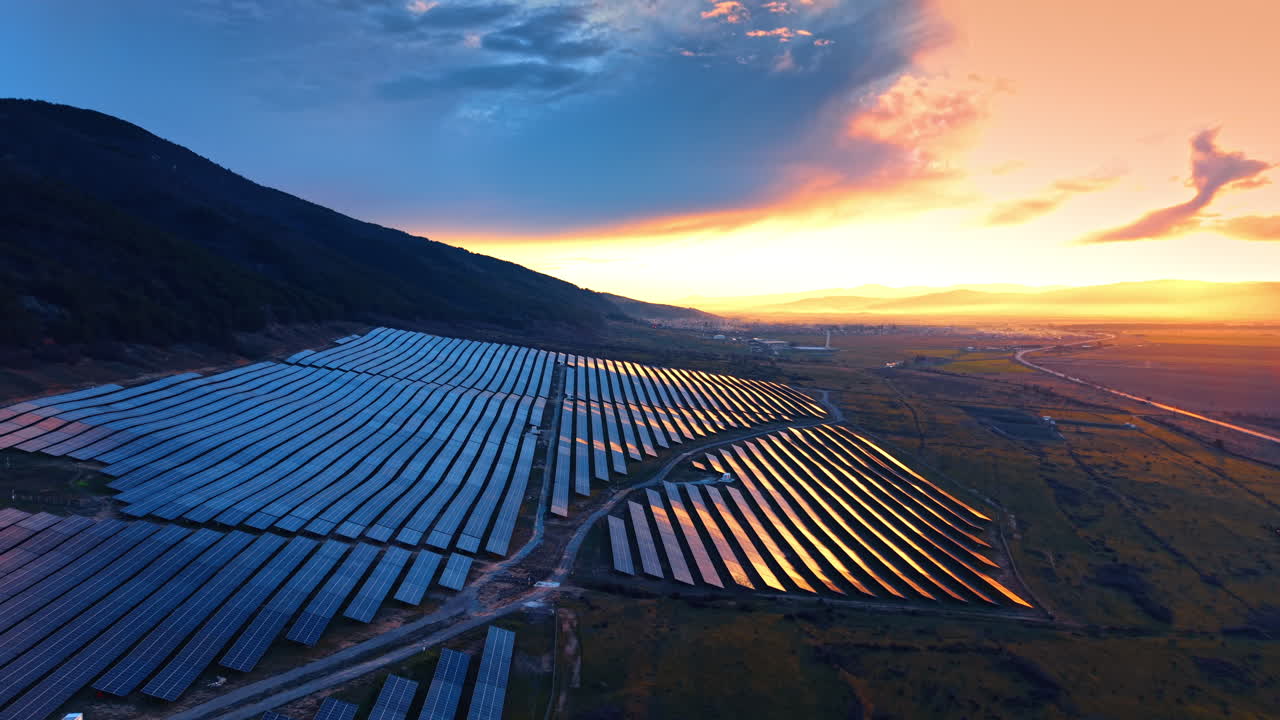 Solnedgang over et solcelleanlæg med refleksioner på panelerne. Oversigtsbillede af en stor solcellepark i skumringen, hvor himlen spejler sig i de fotovoltaiske overflader.