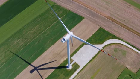 aerial orbit over the modern wind turbine in the middle of the green fields