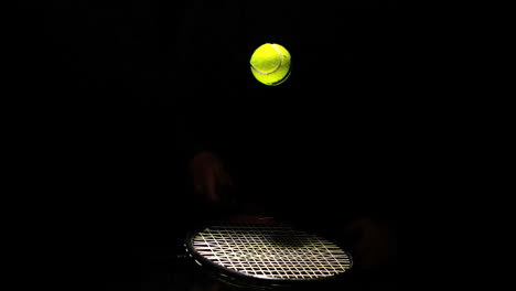 tennis ball bouncing on a racket on black background